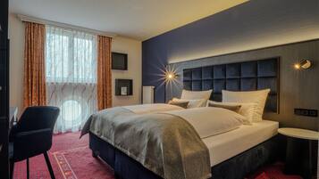Habitación de hotel con una cama grande, un escritorio, una silla, una mesita y una ventana con cortinas.