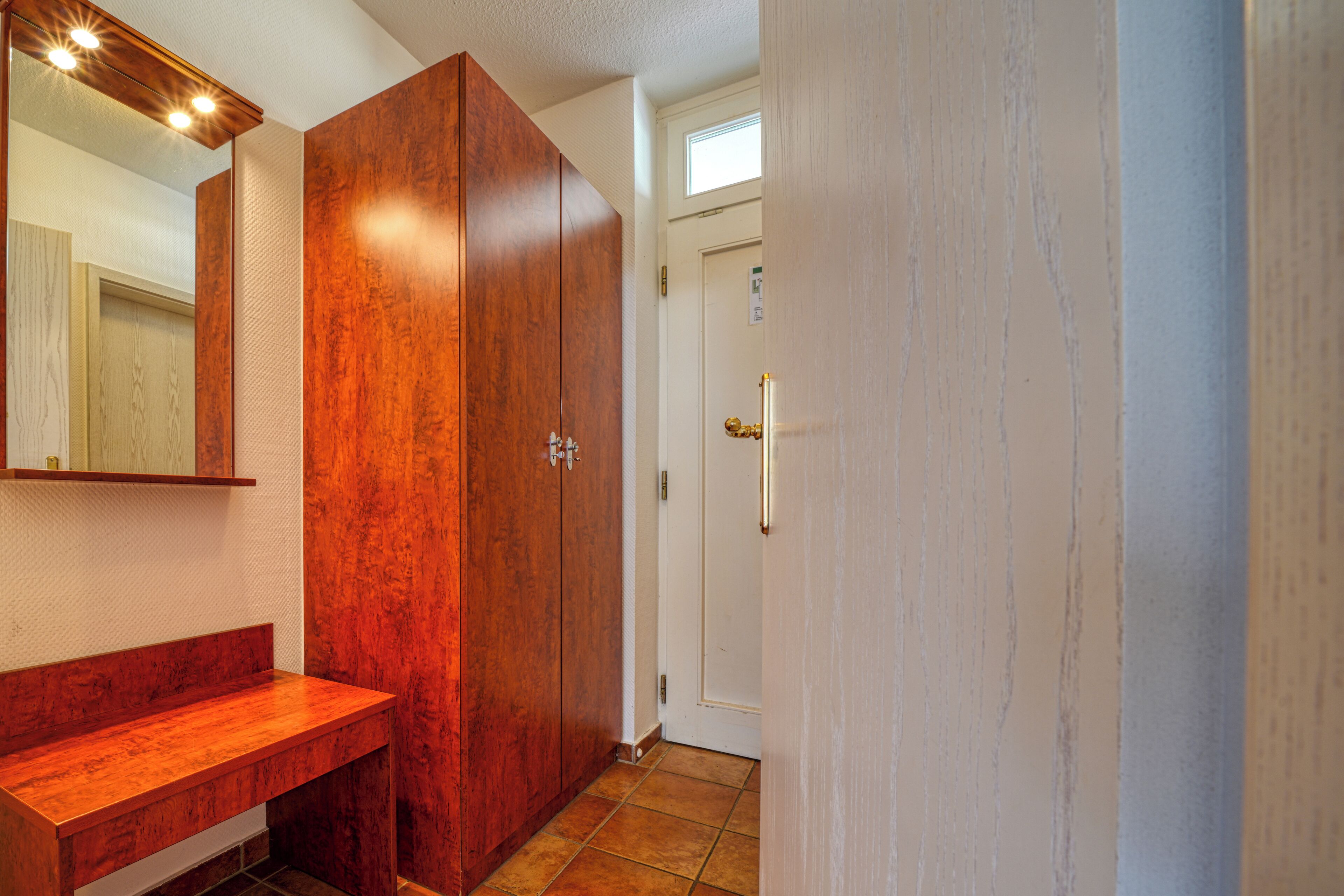 A bathroom with a wooden vanity, a large mirror, and a door leading to another room.