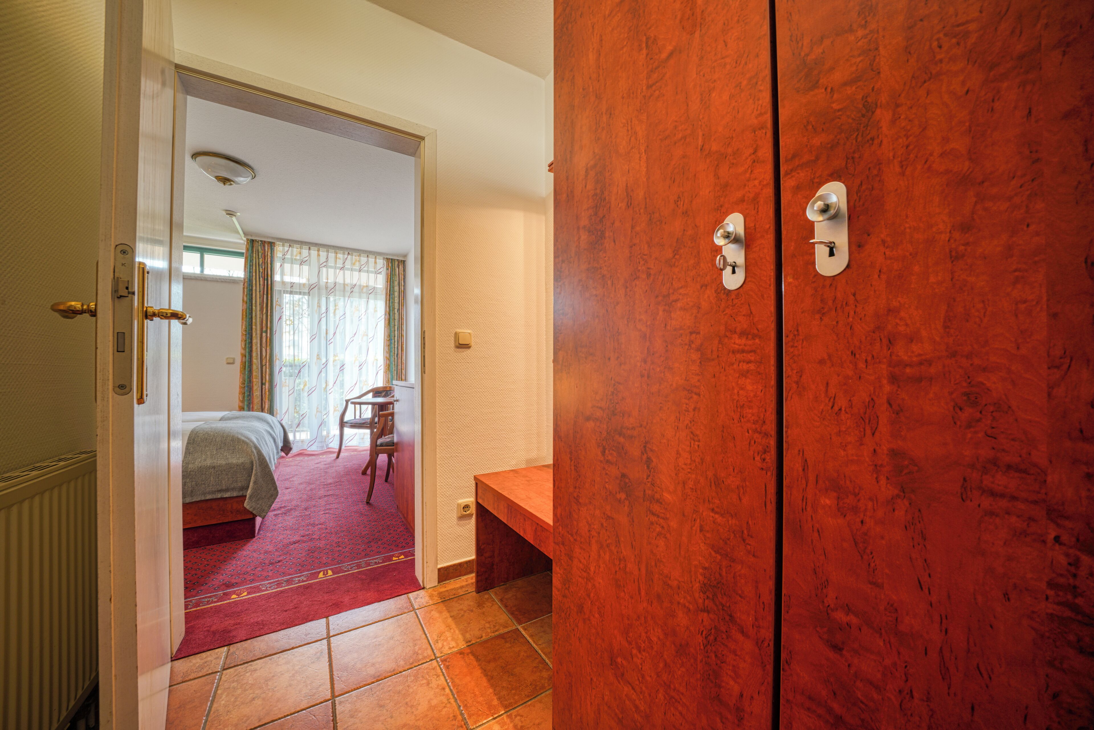 A hotel room with a bed, a wooden wardrobe, and a small desk.