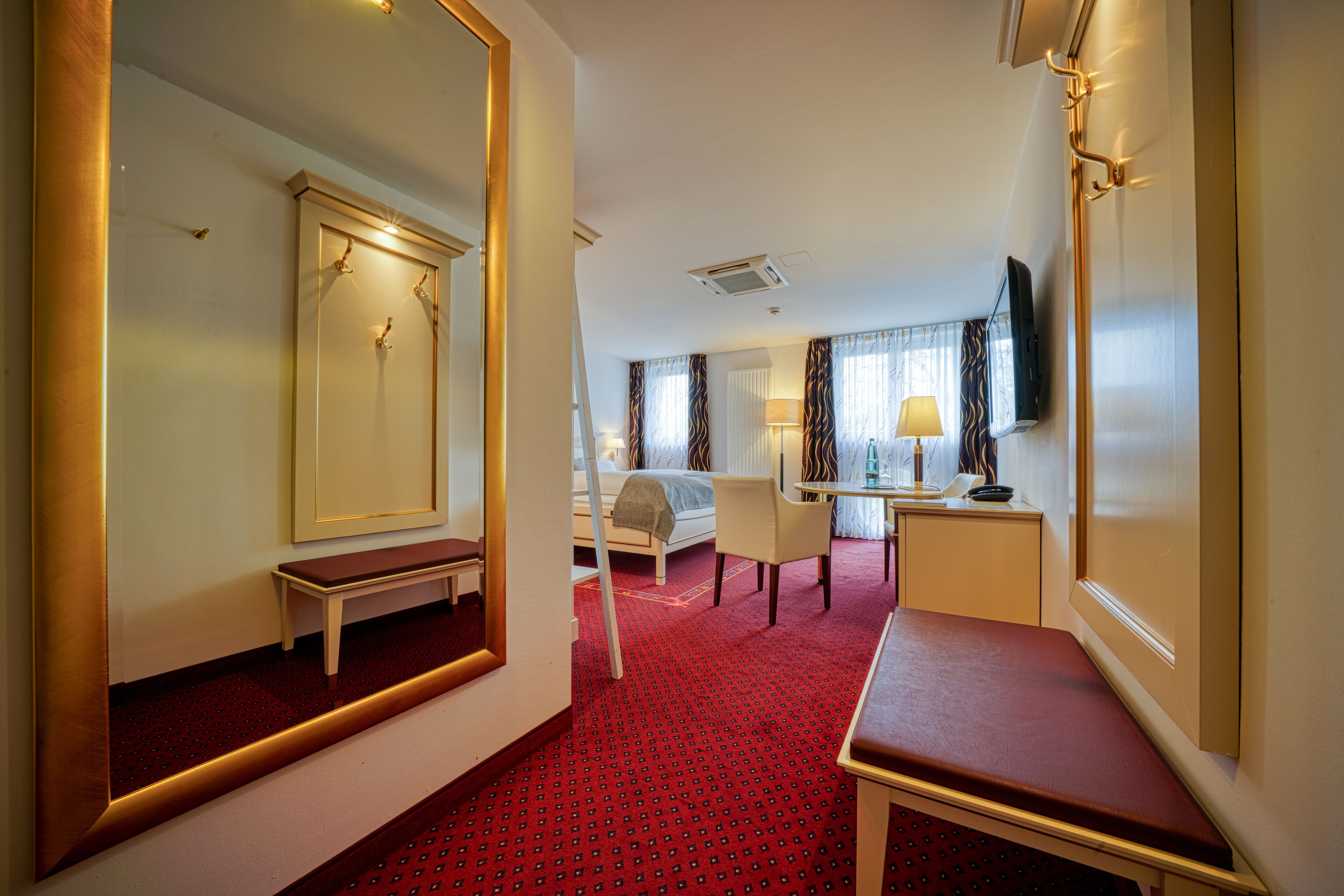 Ein Hotelzimmer mit Bett, Schreibtisch, Stuhl, Spiegel und Fernseher.