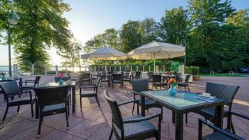 An outdoor patio with wicker furniture, glass tables, and umbrellas providing shade.