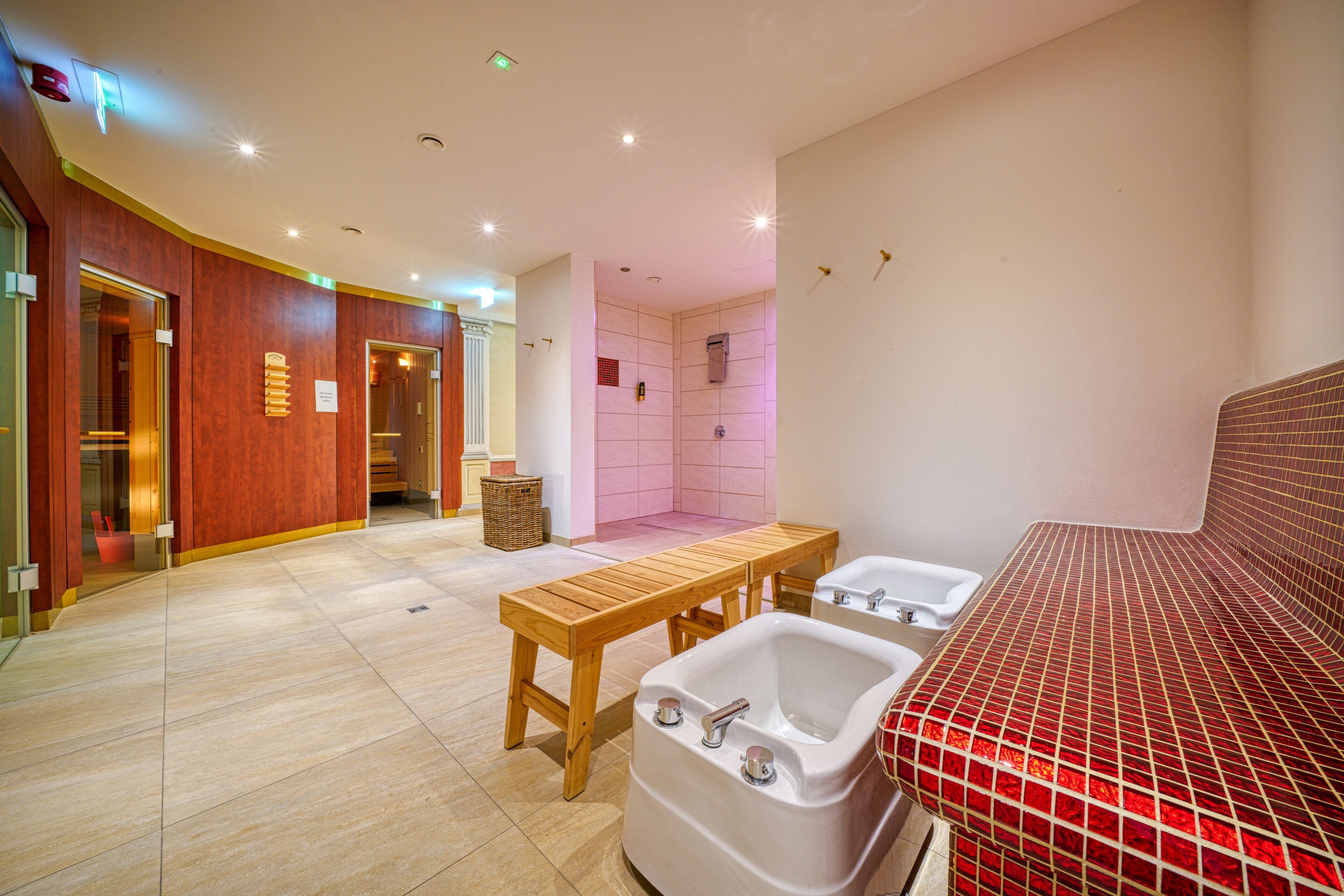 A modern bathroom with a wooden bench, two sinks, and a shower area.