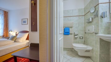 A hotel room with a bed, a desk, a clock, and a bathroom with a toilet, towel dispenser, and hand soap.