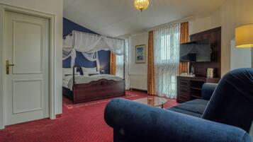 A bedroom with a four-poster bed, a sitting area with a sofa and a coffee table, a dresser, and a television.
