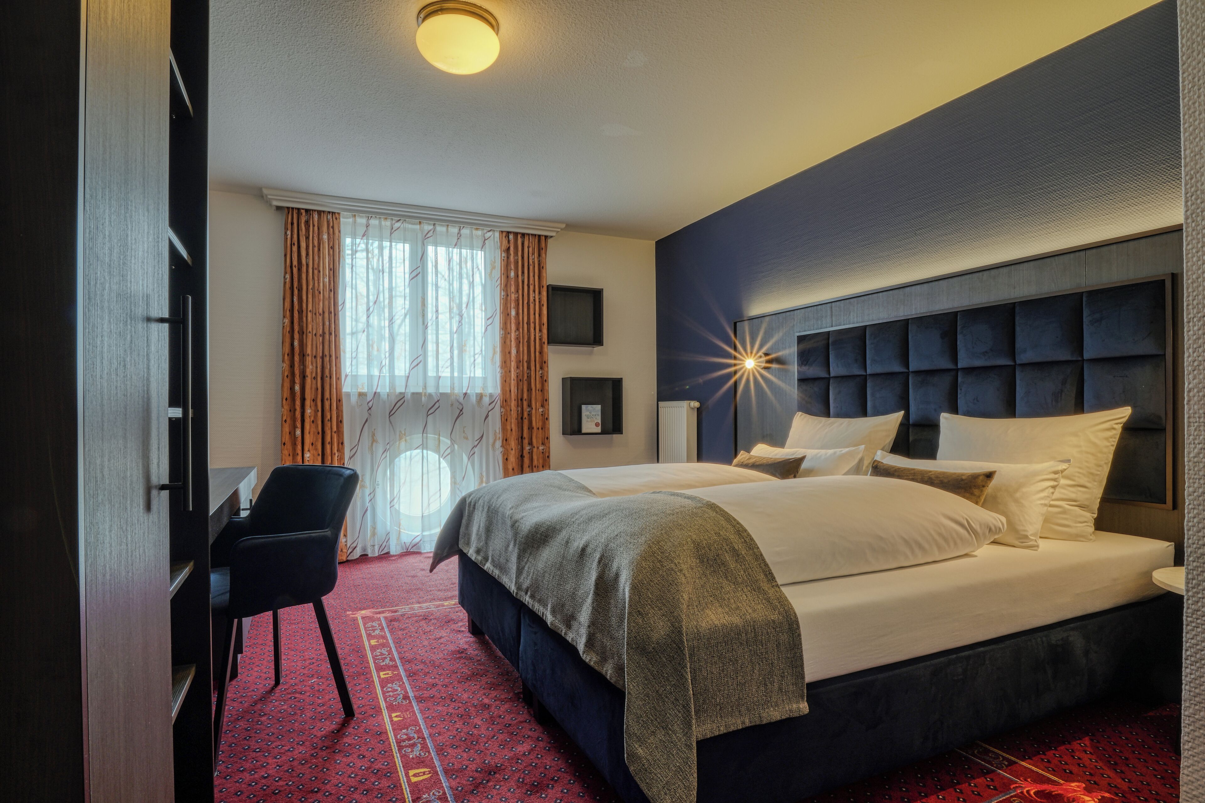 Une chambre d’hôtel avec un lit, un bureau, une chaise et une grande fenêtre avec des rideaux.