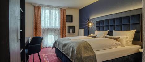 A hotel room with a bed, a desk, a chair, and a large window with curtains.