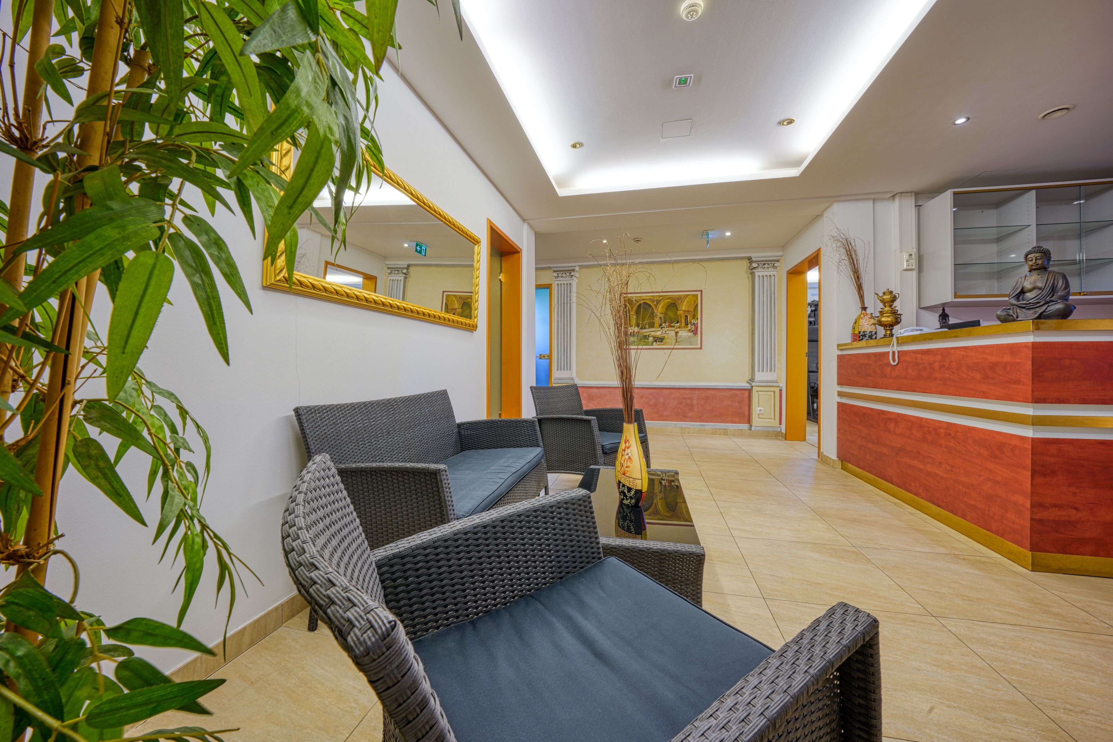 A lobby with wicker furniture, a reception desk, and a Buddha statue.