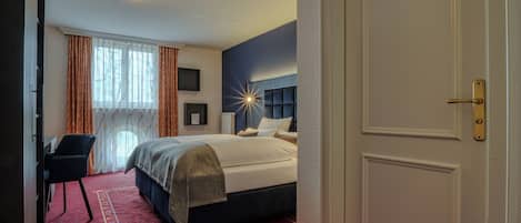 Una habitación de hotel con cama, escritorio, silla, ventana con cortinas y puerta.
