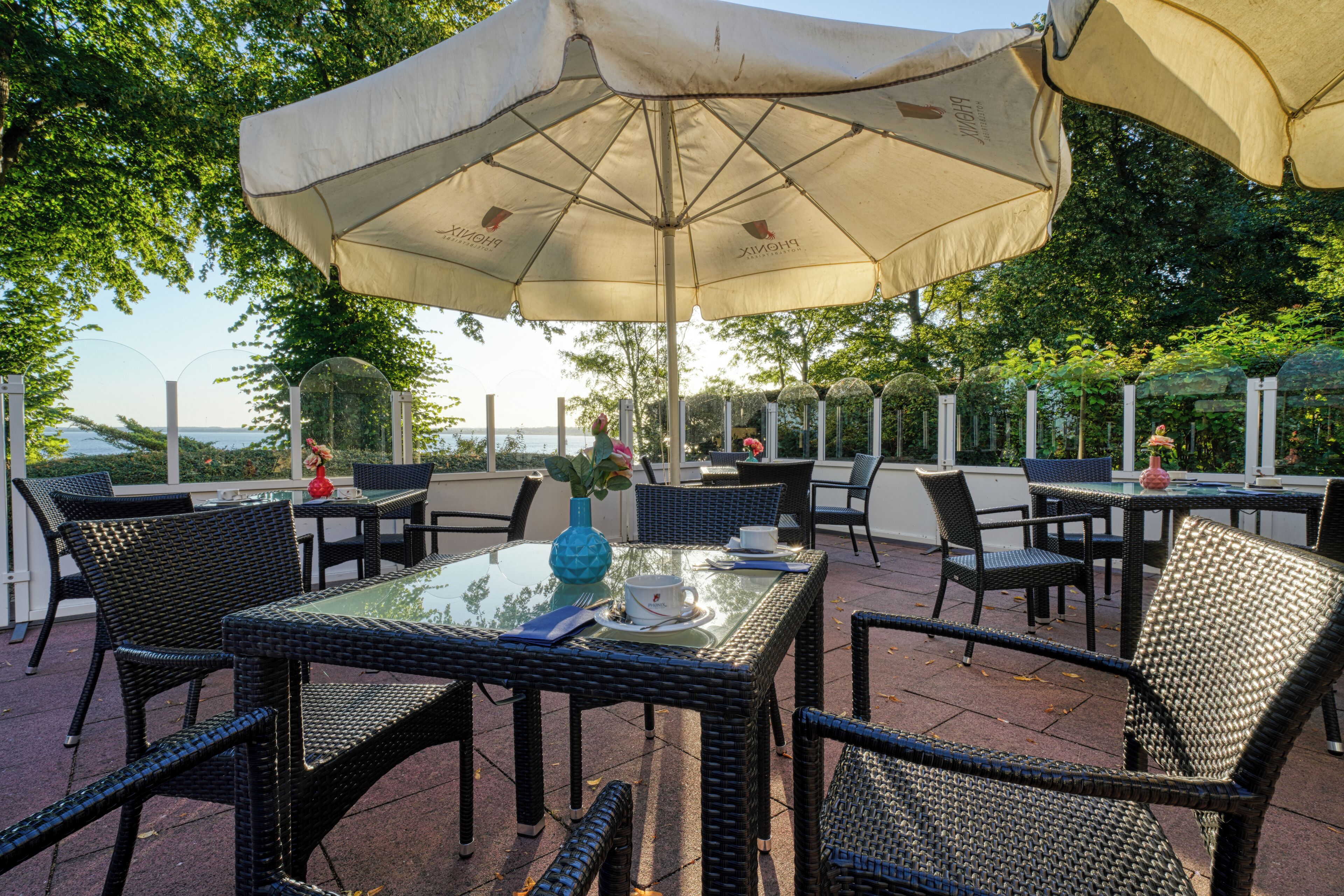 Un espace extérieur aménagé en terrasse, avec des meubles en osier, une table à plateau en verre et un grand parasol pour créer de l’ombre.