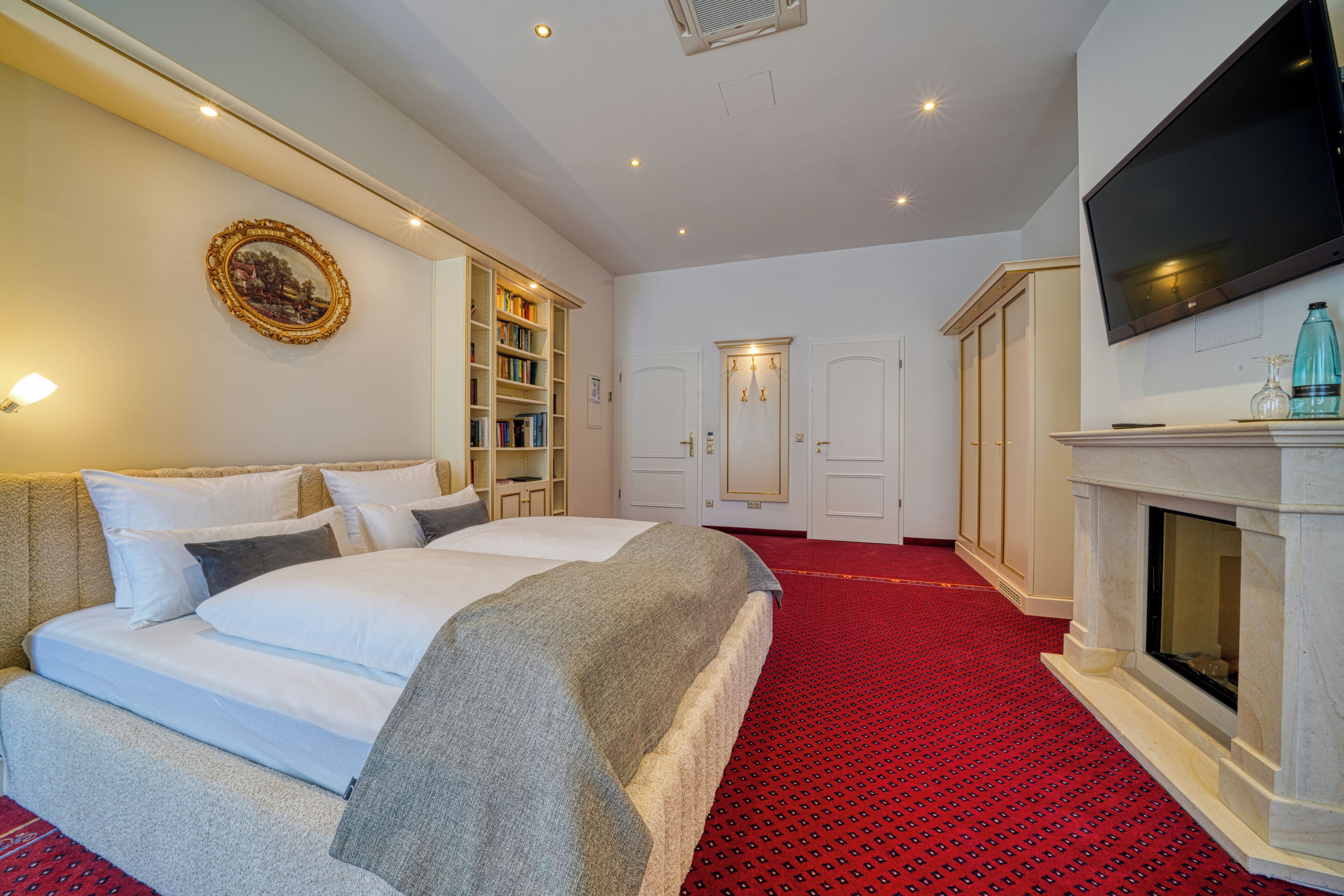 A hotel room with a large bed, a fireplace, a television, and a bookshelf.