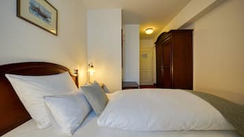 Una cama bien hecha con sábanas y almohadas blancas, un cabecero de madera, una lámpara de noche y un cuadro en la pared.