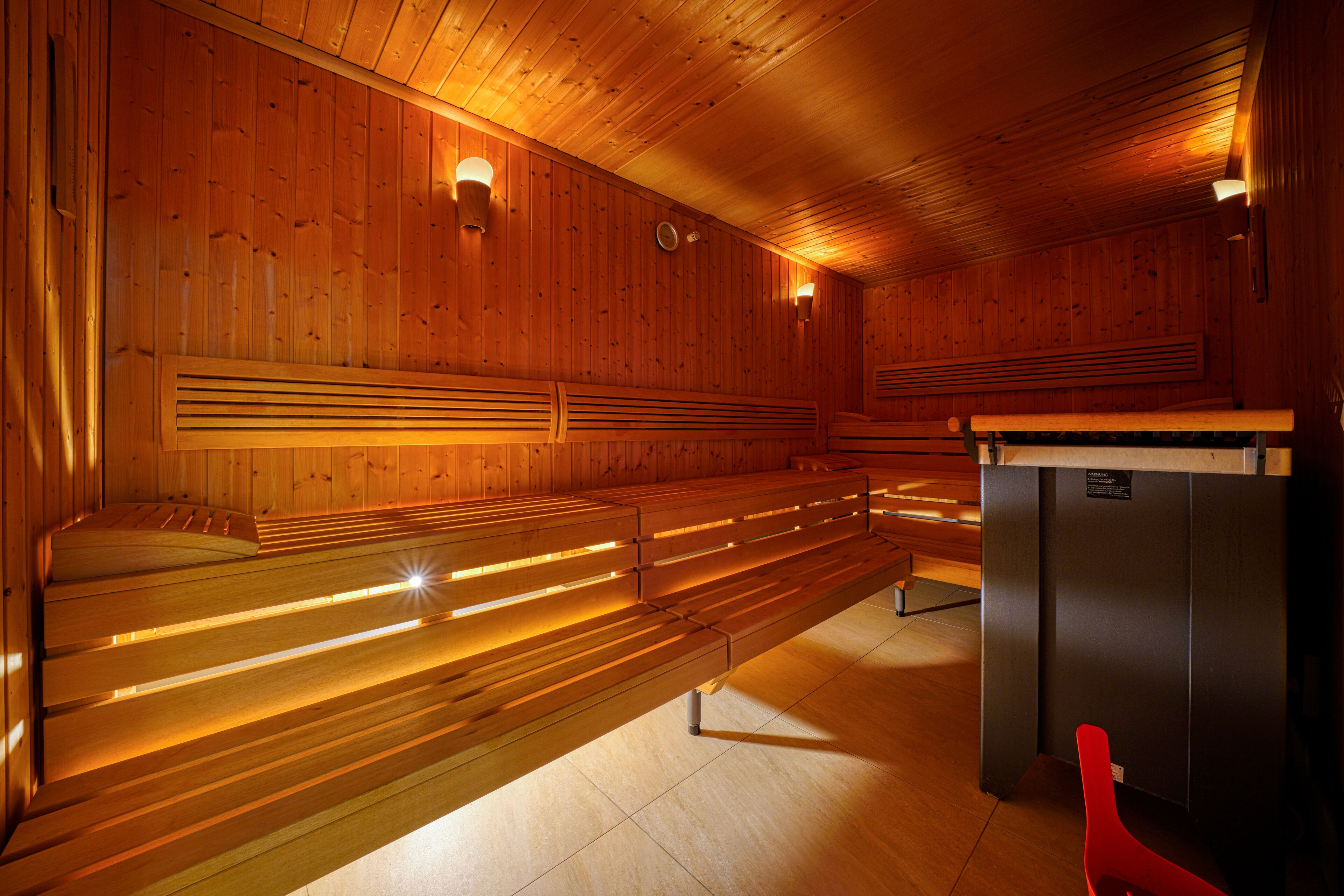 A sauna with wooden benches and walls, a bench heater, and a small table with a sign.