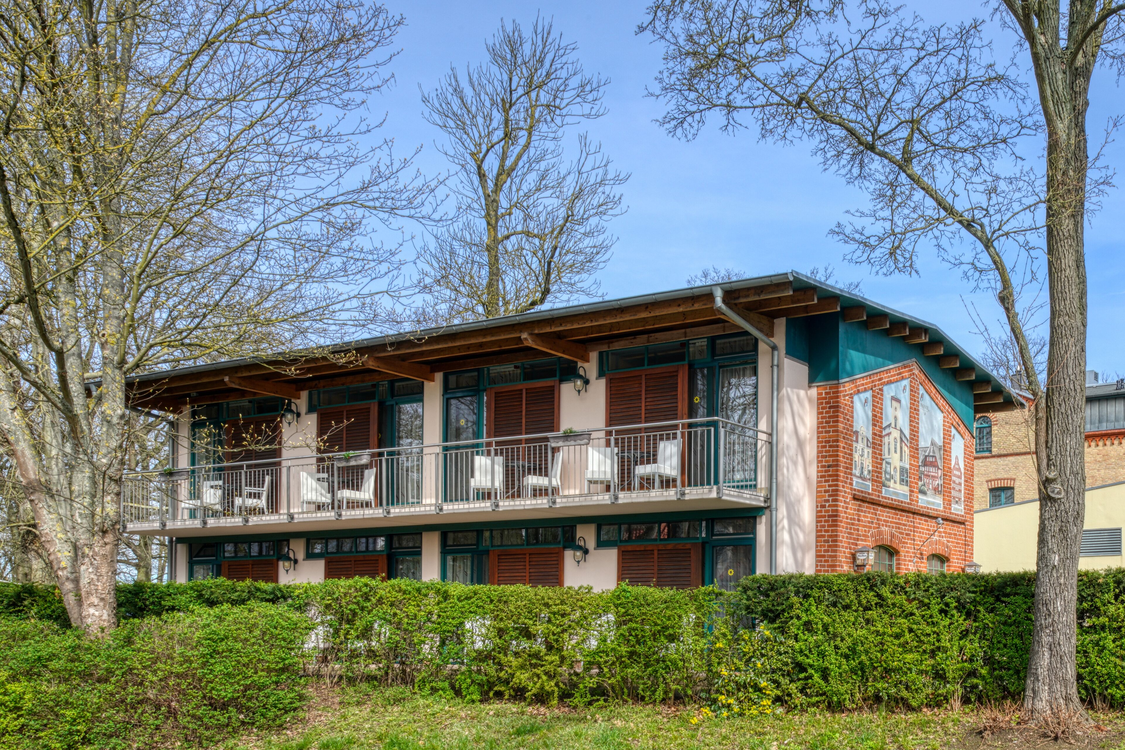 A two-story building with a balcony, surrounded by trees and greenery.