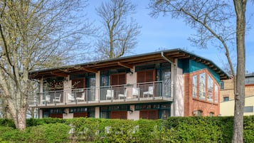 A two-story building with a balcony, surrounded by trees and greenery.