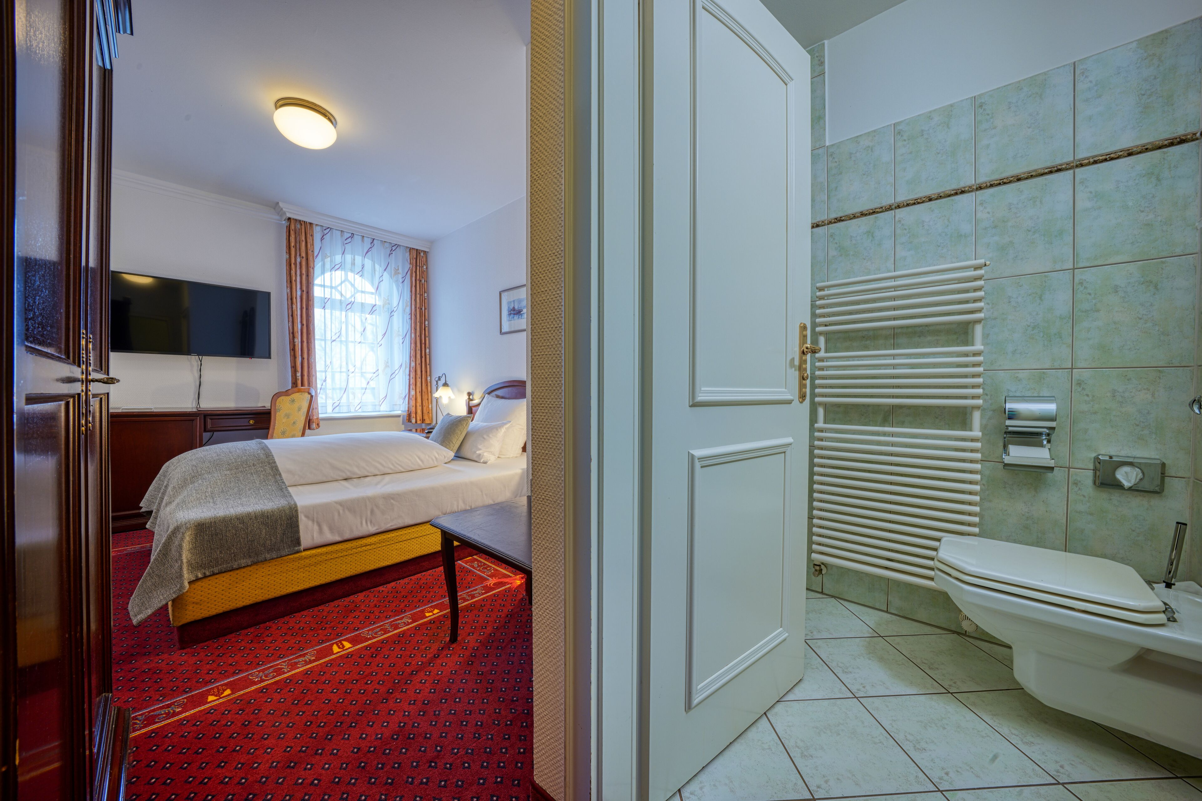 Una habitación de hotel con una cama, mesita de noche y un televisor fijado a la pared.