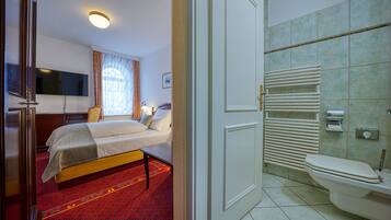Una habitación de hotel con una cama, mesita de noche y un televisor fijado a la pared.