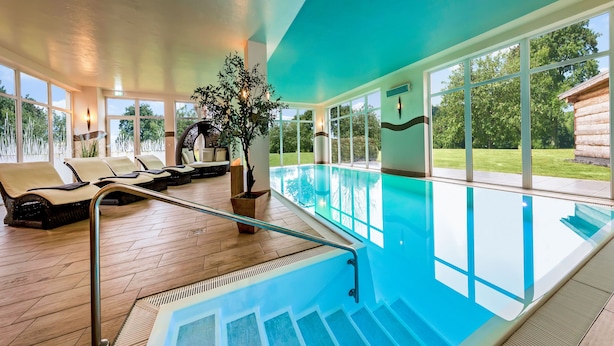 A swimming pool area with a glass-enclosed deck, lounge chairs, and a staircase leading to the pool. - Land-gut-Hotel Hermann (Bentwisch)