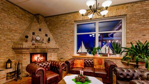 A cozy living room with leather sofas, a fireplace, and a large window overlooking a cityscape. - Land-gut-Hotel Hermann (Bentwisch)