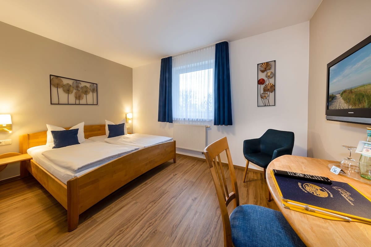 A hotel room with a wooden bed, a desk with a chair, a television, and artwork on the walls.