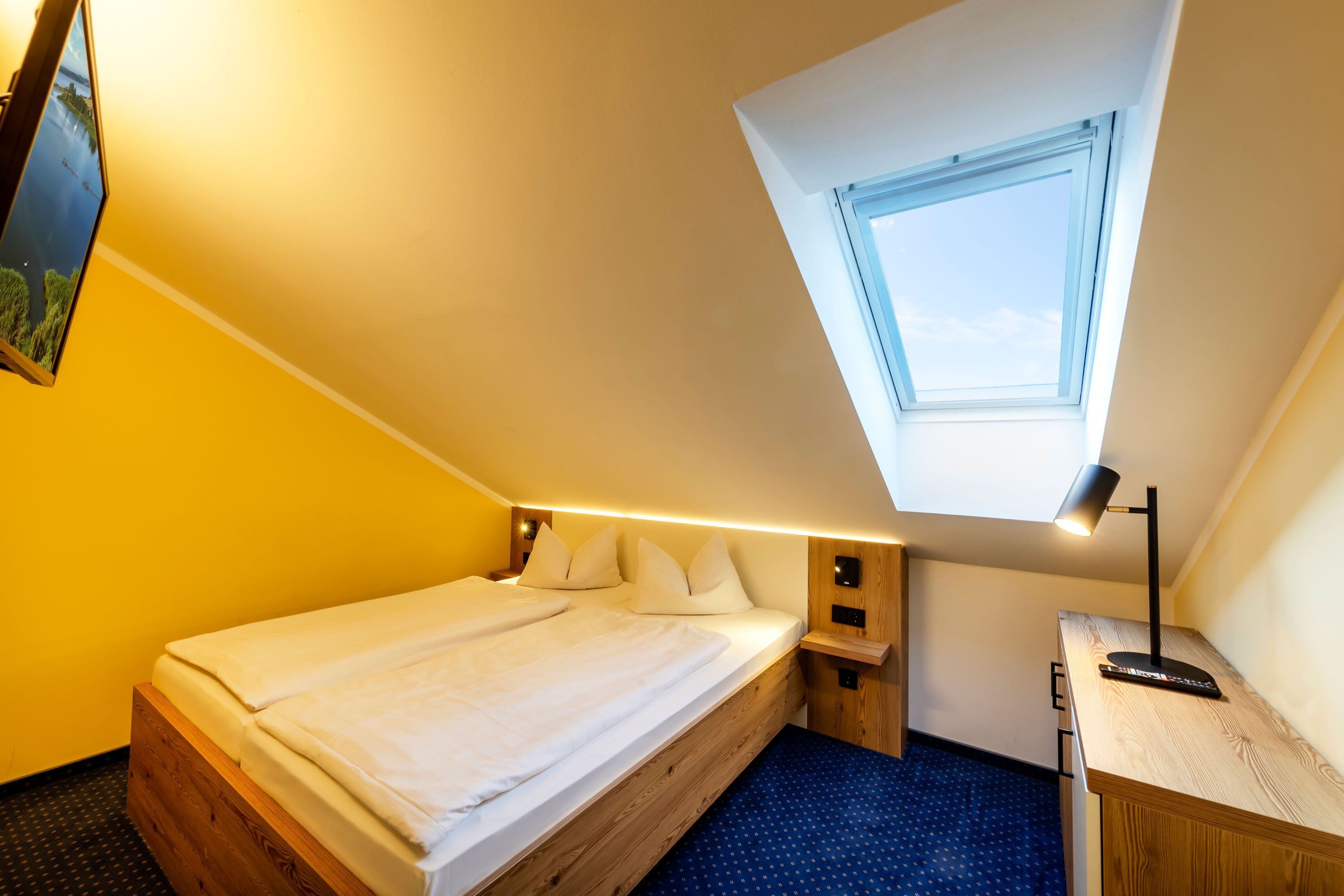 A small, well-lit room with a bed, a desk, and a skylight.