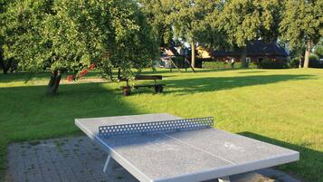 A ping pong table in a park with trees and a house in the background.