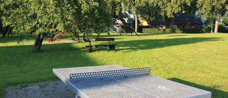 A ping pong table in a park with trees and a house in the background.