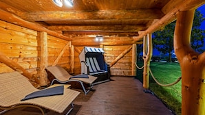 A wooden cabin with a deck, lounge chairs, and a barbecue grill. - Land-gut-Hotel Hermann (Bentwisch)
