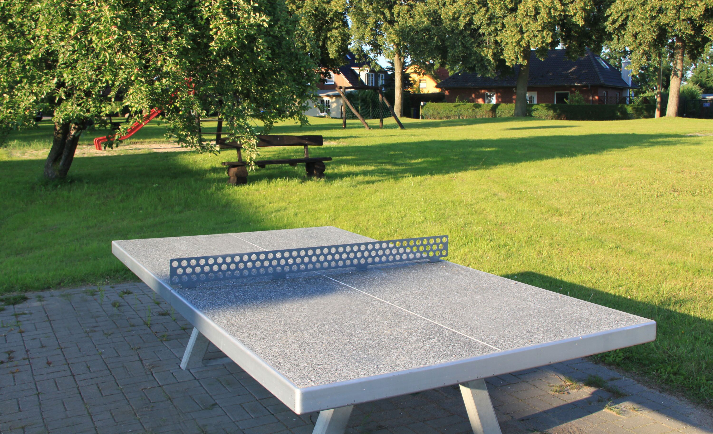 A table tennis table in a park with a picnic table and a swing set in the background.