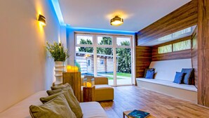 A modern living room with a sofa, a small table, and a view of a wooden cabin through large windows. - Land-gut-Hotel Hermann (Bentwisch)