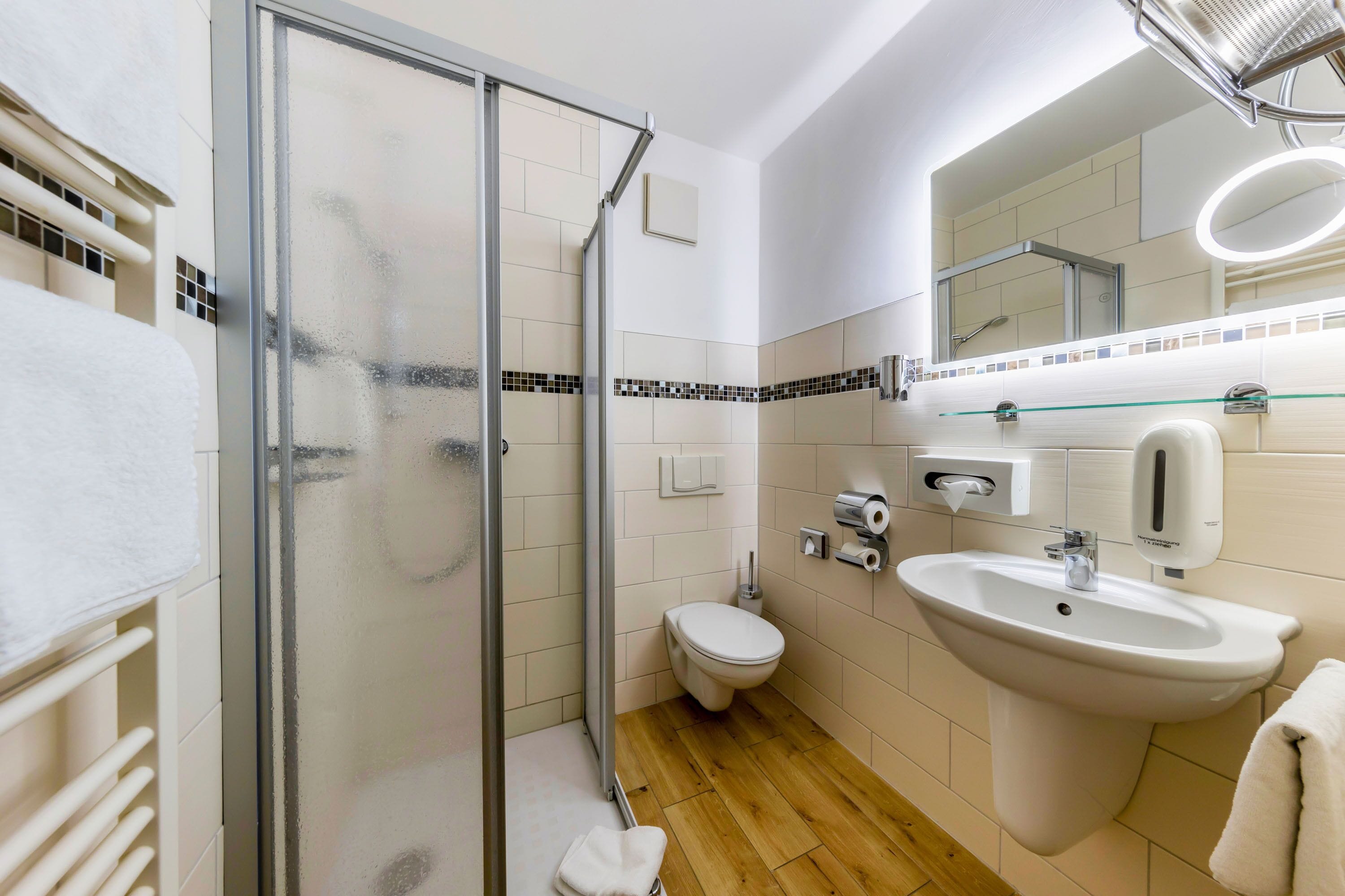 Une salle de bain moderne avec une douche à parois de verre, des toilettes, un lavabo et un miroir avec éclairage intégré.