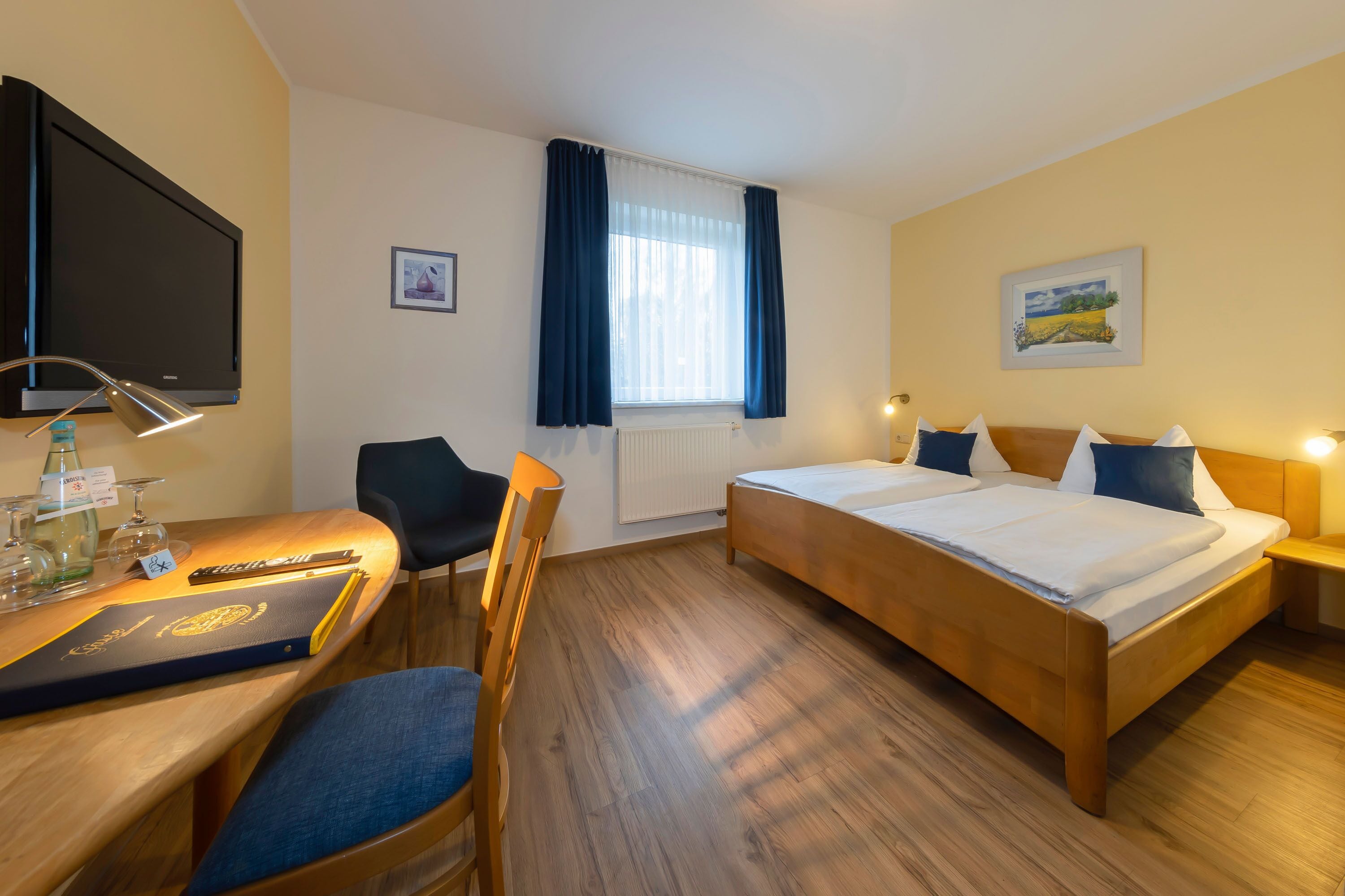 Een hotelkamer met een bed, een bureau met stoel, een televisie en een raam met gordijnen.