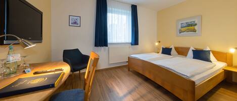 Een hotelkamer met een bed, een bureau met stoel, een televisie en een raam met gordijnen.