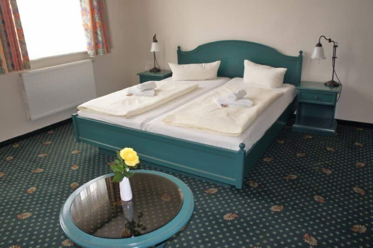 Ein Doppelbett mit weißen Leinentüchern, zwei Nachttische mit Lampen, eine Vase mit einer gelben Blume und ein gemustertes Teppich.