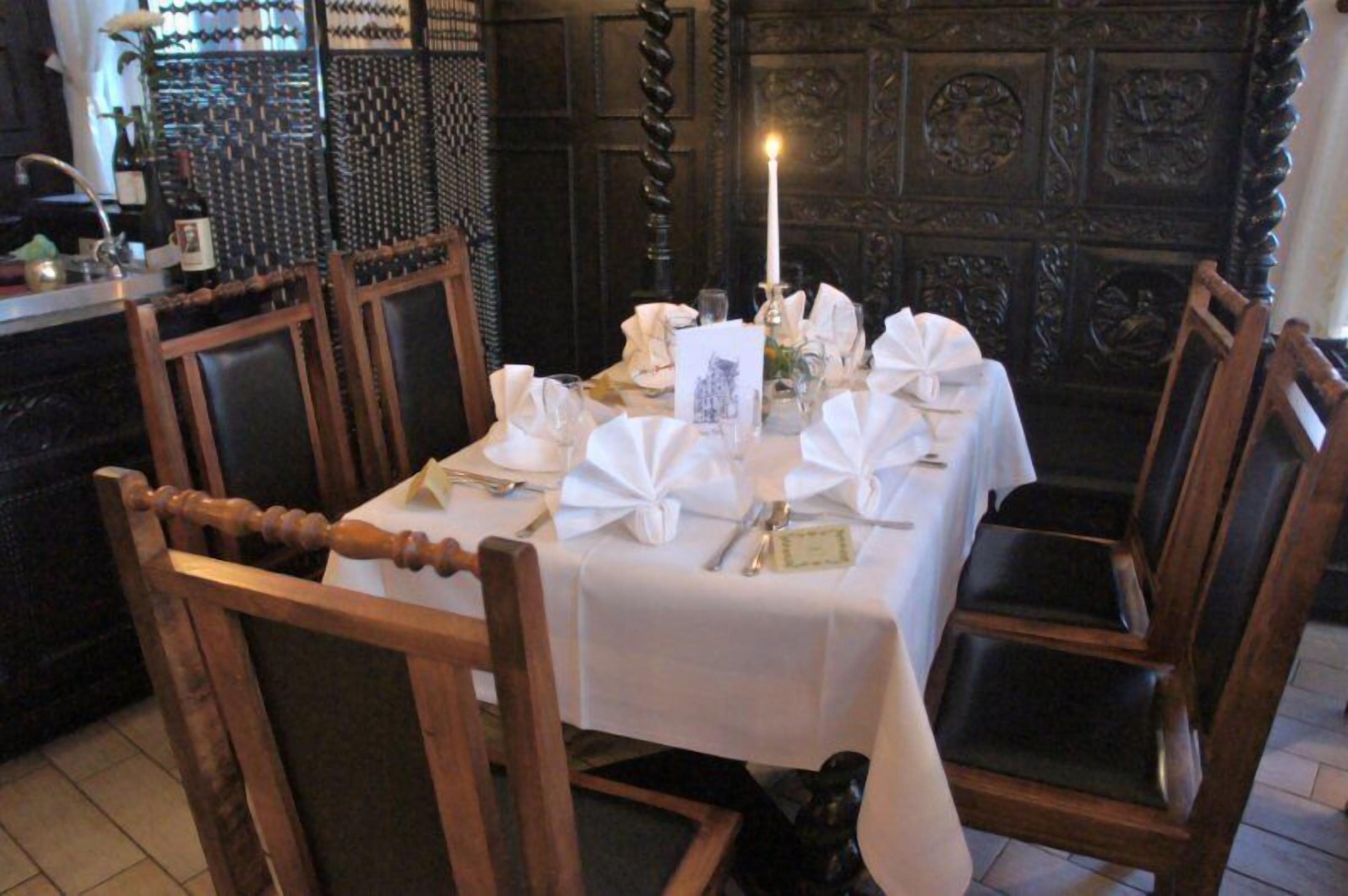 A dining table set for four with white tablecloths, folded napkins, and silverware.