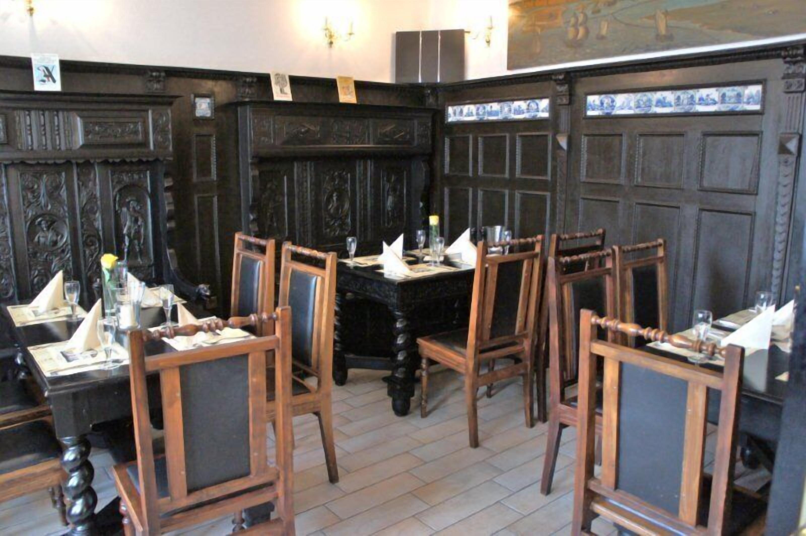 A dining area with wooden chairs and tables, dark wood paneling, and a tiled backsplash.