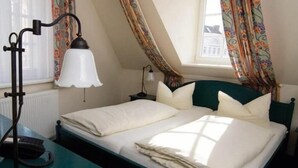A bedroom with a bed, a desk with a lamp, a telephone, and a window with curtains. - Hotel und ReuterHaus (Wismar)