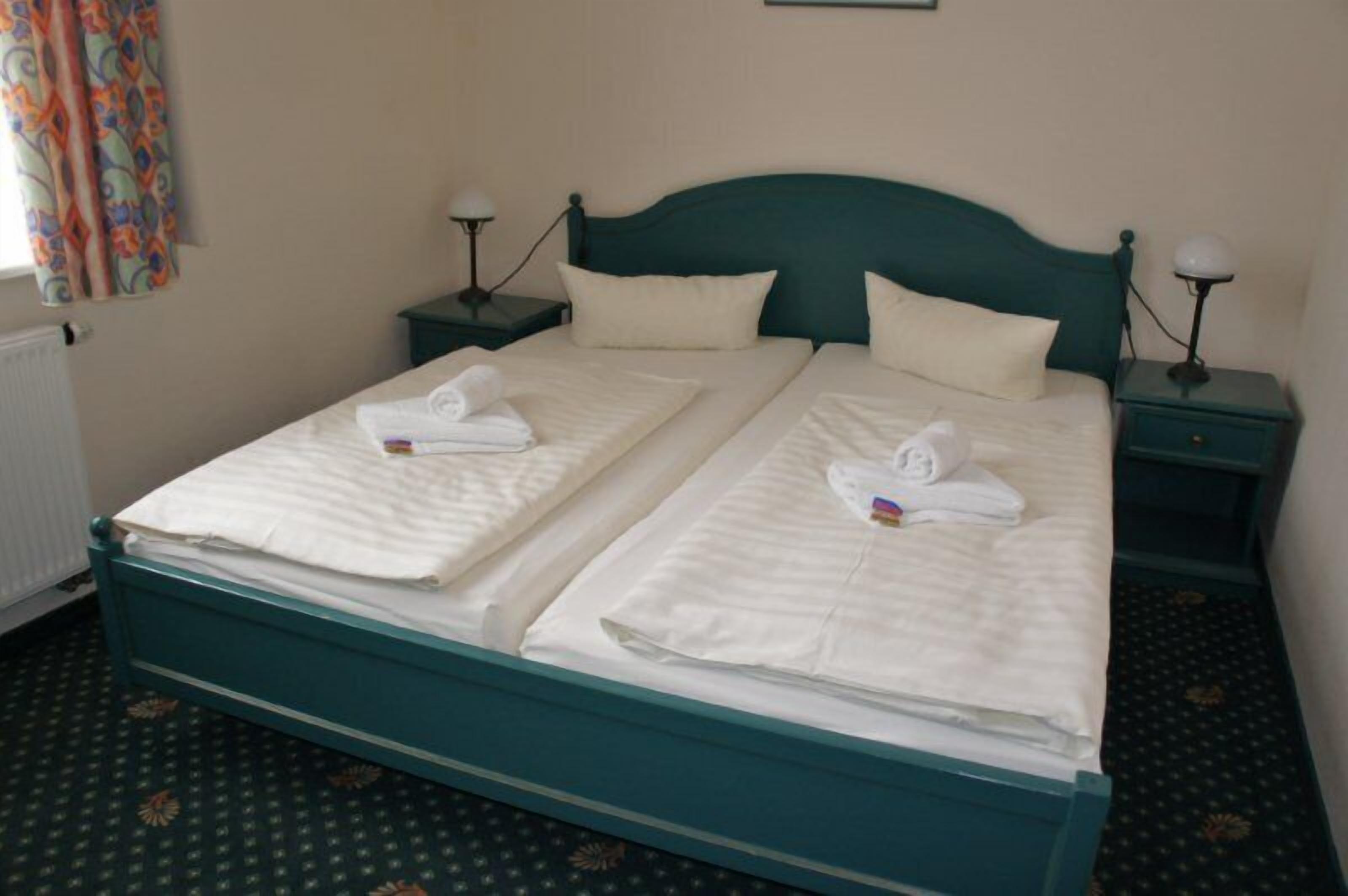 A double bed with two nightstands, each with a lamp, in a room with patterned carpet.