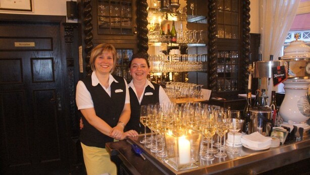 Two staff members at a bar with a large number of wine glasses and a candle. - Hotel und ReuterHaus (Wismar)
