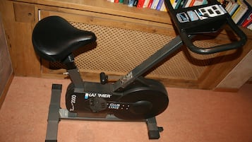 Een stilstaande hometrainer met een zwart zadel en handvatten, op een houten vloer met een geperforeerd houten paneel op de achtergrond.