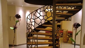 Een spiraaltrap met een geometrische metalen balustrade, houten treden en een houten leuning.