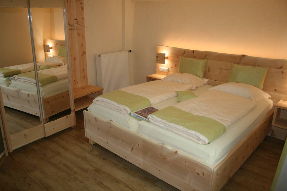 Un lit double avec une tête de lit en bois, deux tables de chevet avec des lampes, un miroir et un radiateur.