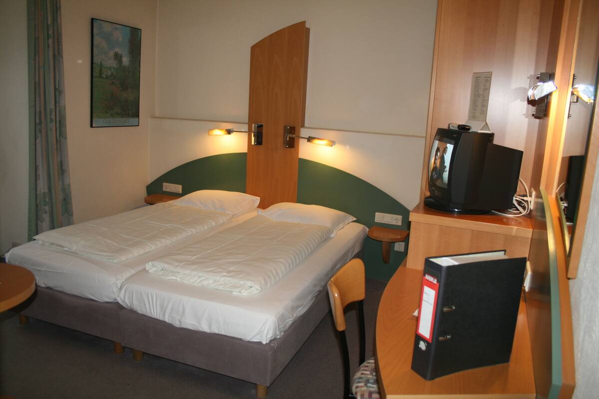 Une chambre d’hôtel équipée d’un lit double, d’un bureau avec un ordinateur, d’une télévision et d’une bibliothèque.