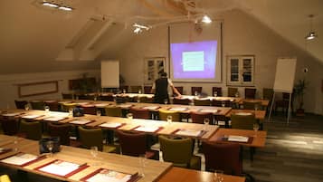 Un salón de conferencias con varias mesas, sillas y una pantalla para presentaciones.