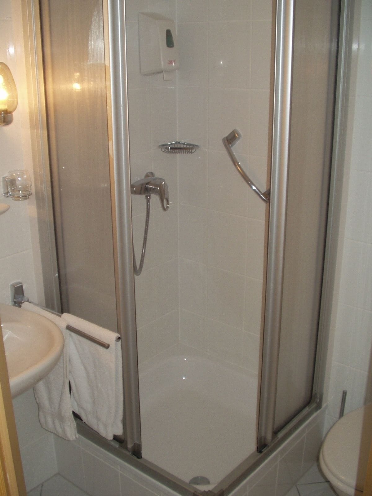 Un bany amb plat de dutxa tancat amb vidre, un lavabo i un vàter.