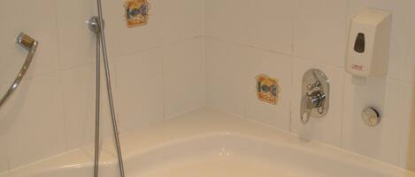 A bathtub with a handheld showerhead, a soap dispenser, and a small decorative tile above it.