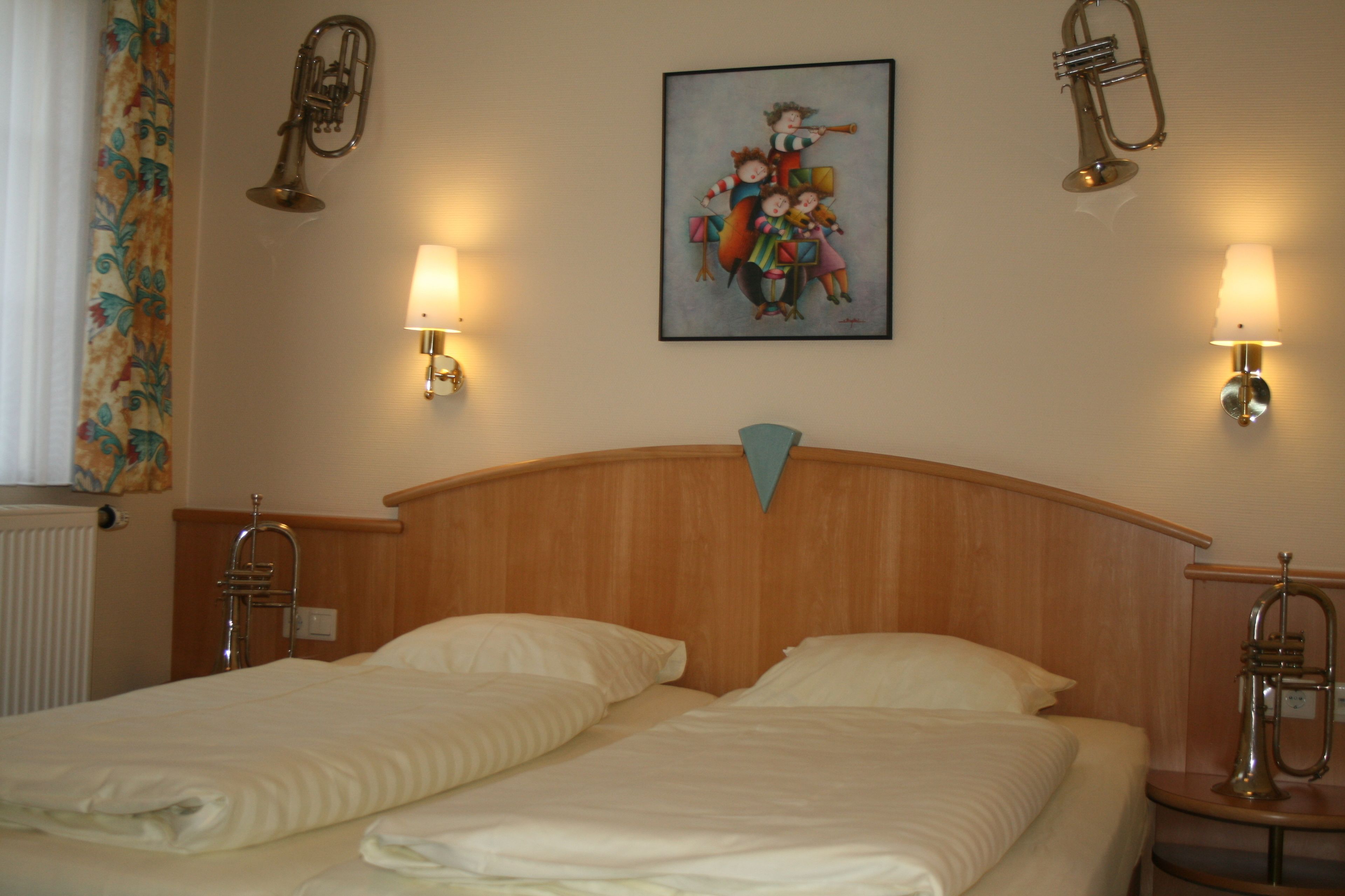 A hotel room with two beds, a wooden headboard, wall-mounted lamps, and a painting above the beds.