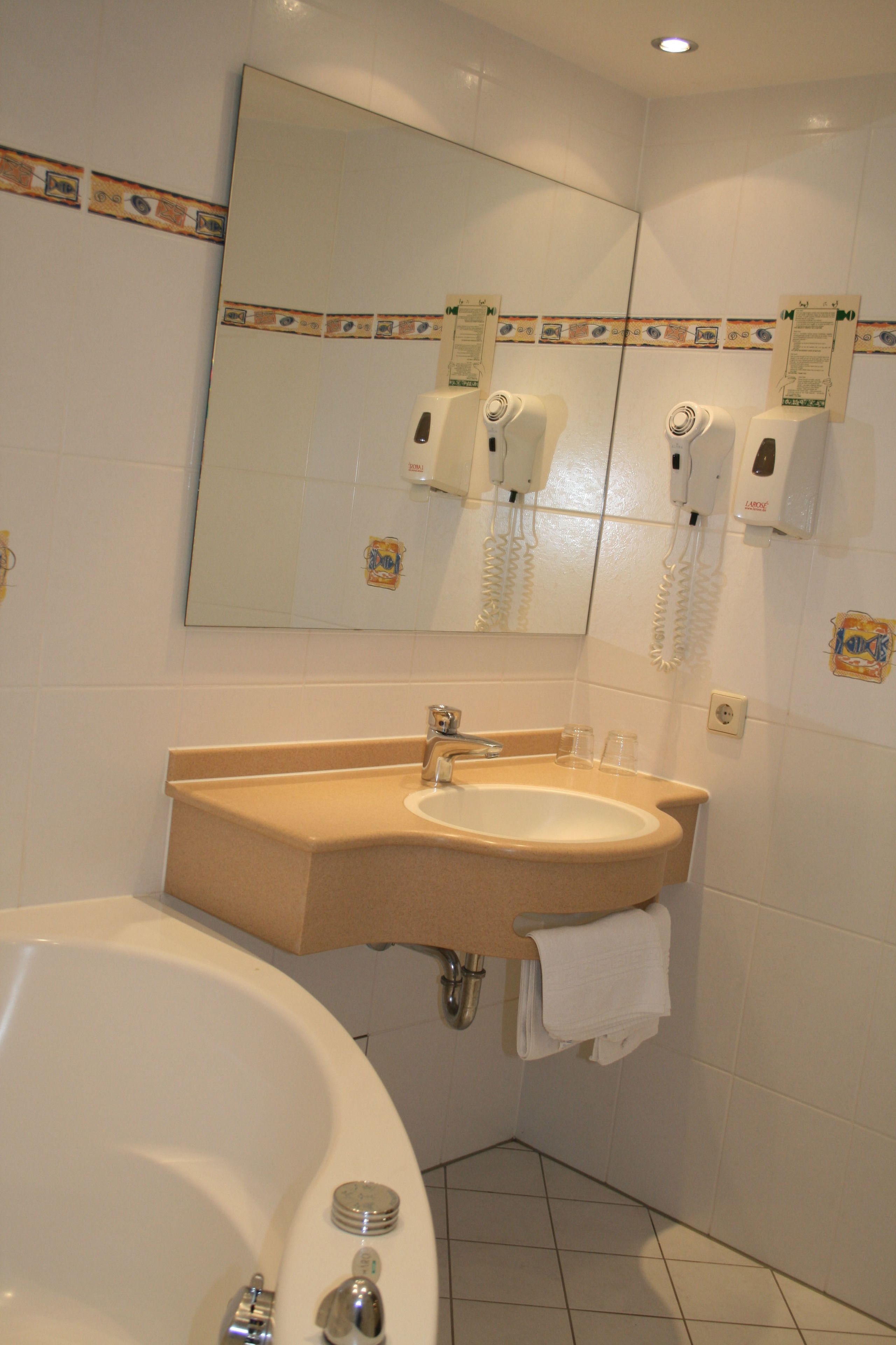 Une salle de bain équipée d’un lavabo, d’un miroir et d’un sèche-cheveux fixé au mur.