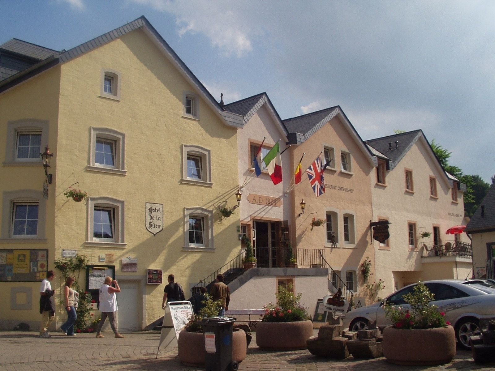 A building with multiple windows, a sign for 'Hotel de la Cure', and flags.