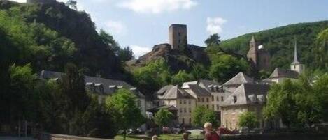 Uma cidade histórica com uma torre imponente numa colina, rodeada por vegetação exuberante e edifícios tradicionais.