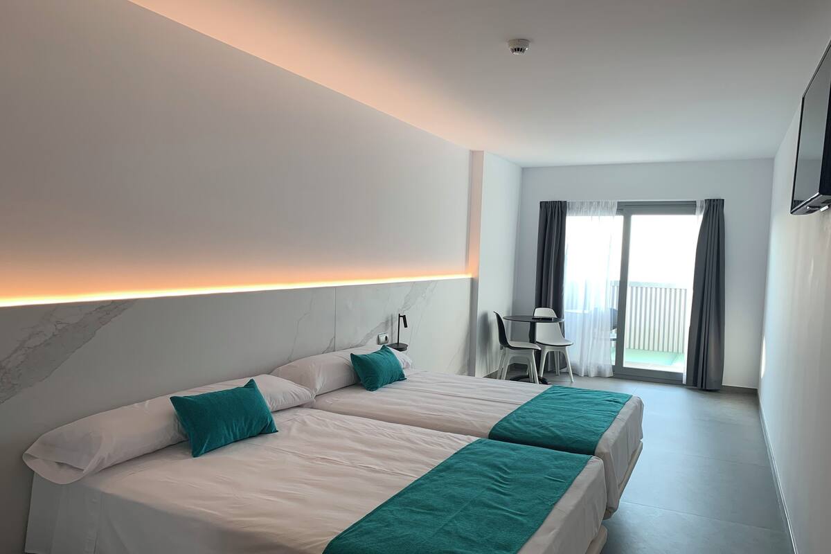 A hotel room with two beds, a desk, and a balcony.